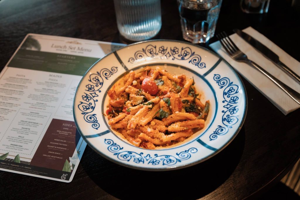 Casarecce Del Giardino pasta served at Marzano Italian Grill in York, topped with parmesan and fresh vegetables, with the lunch set menu visible in the background.