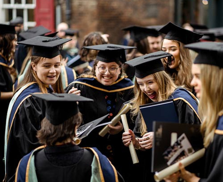 University graduates celebrating their graduation day with diplomas and academic gowns, gathered together after a ceremony in York. Perfect for Marzano's student discount and graduation dining offers.
